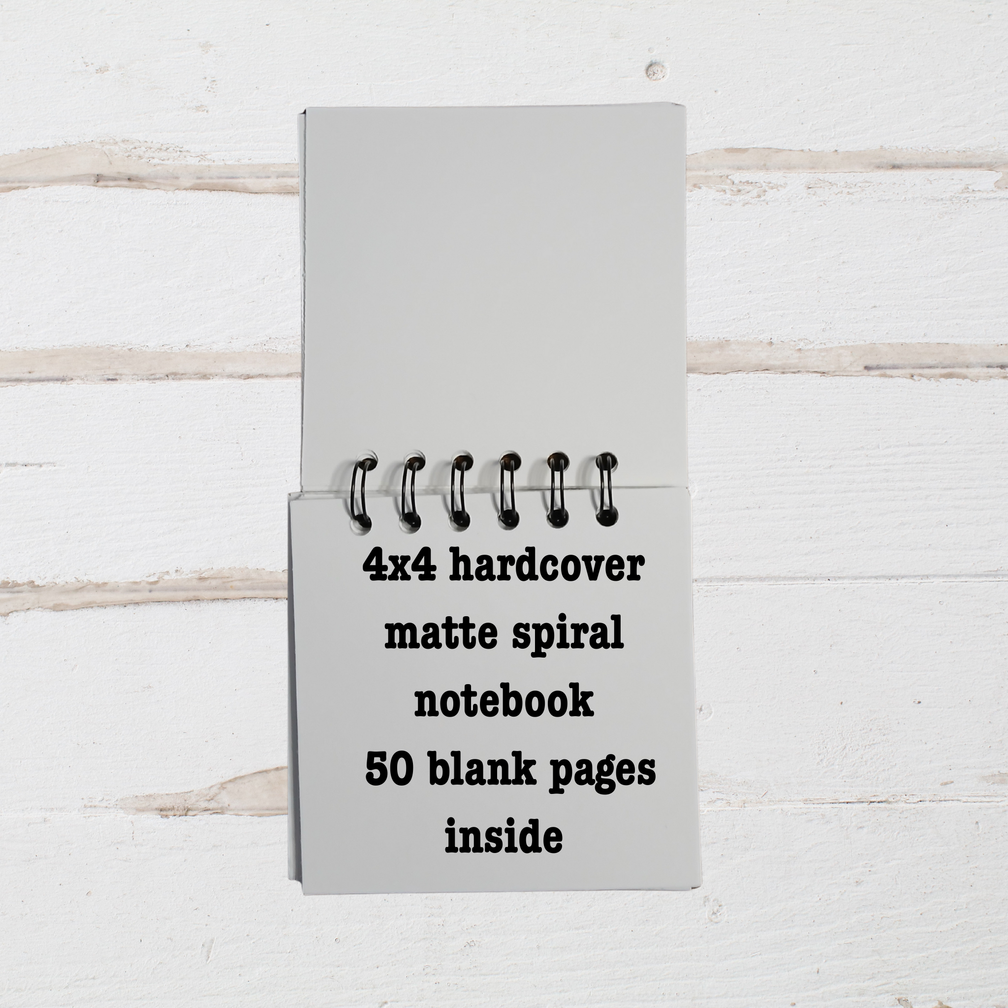 Gray 4x4 hardcover matte spiral notebook with text on a white wooden background