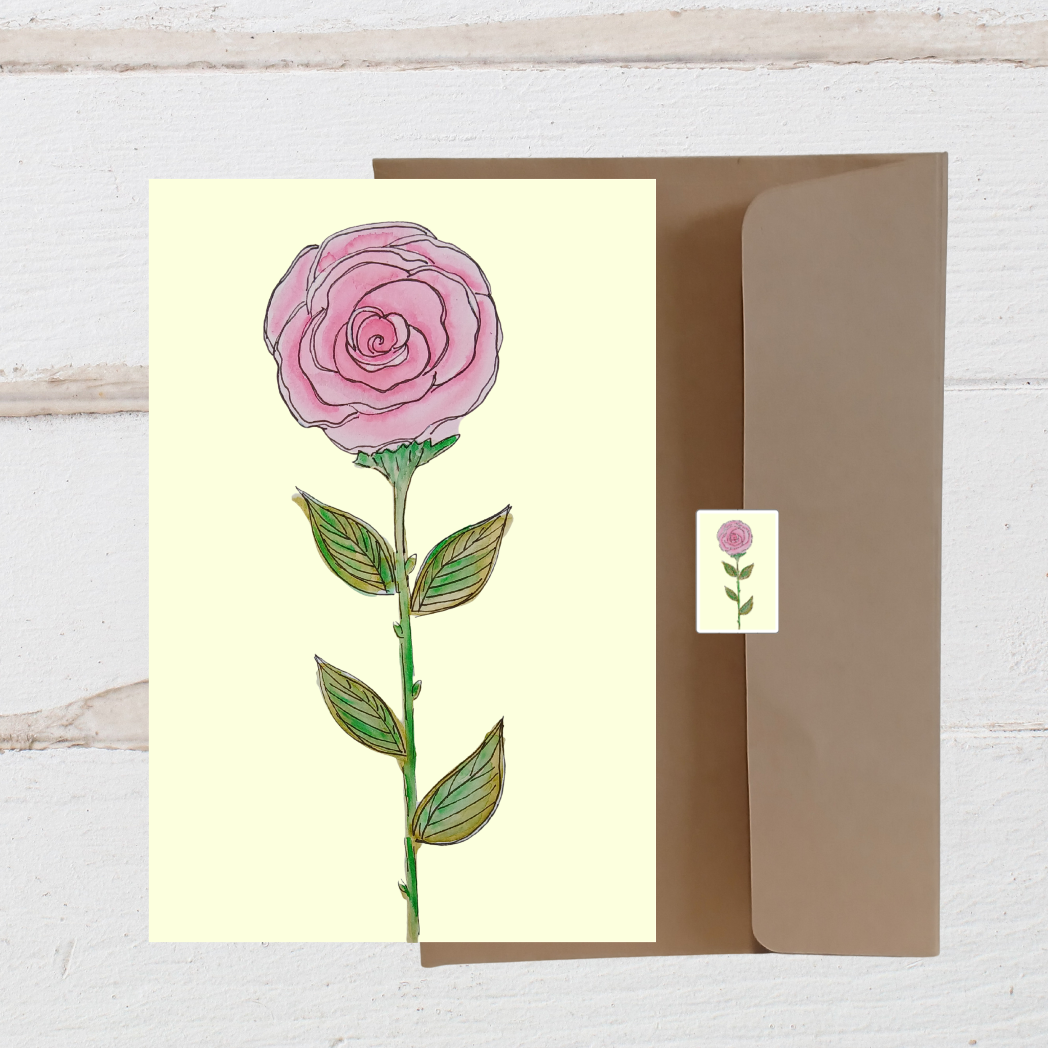 Greeting card with a pink rose illustration on a light yellow background, accompanied by a matching envelope.