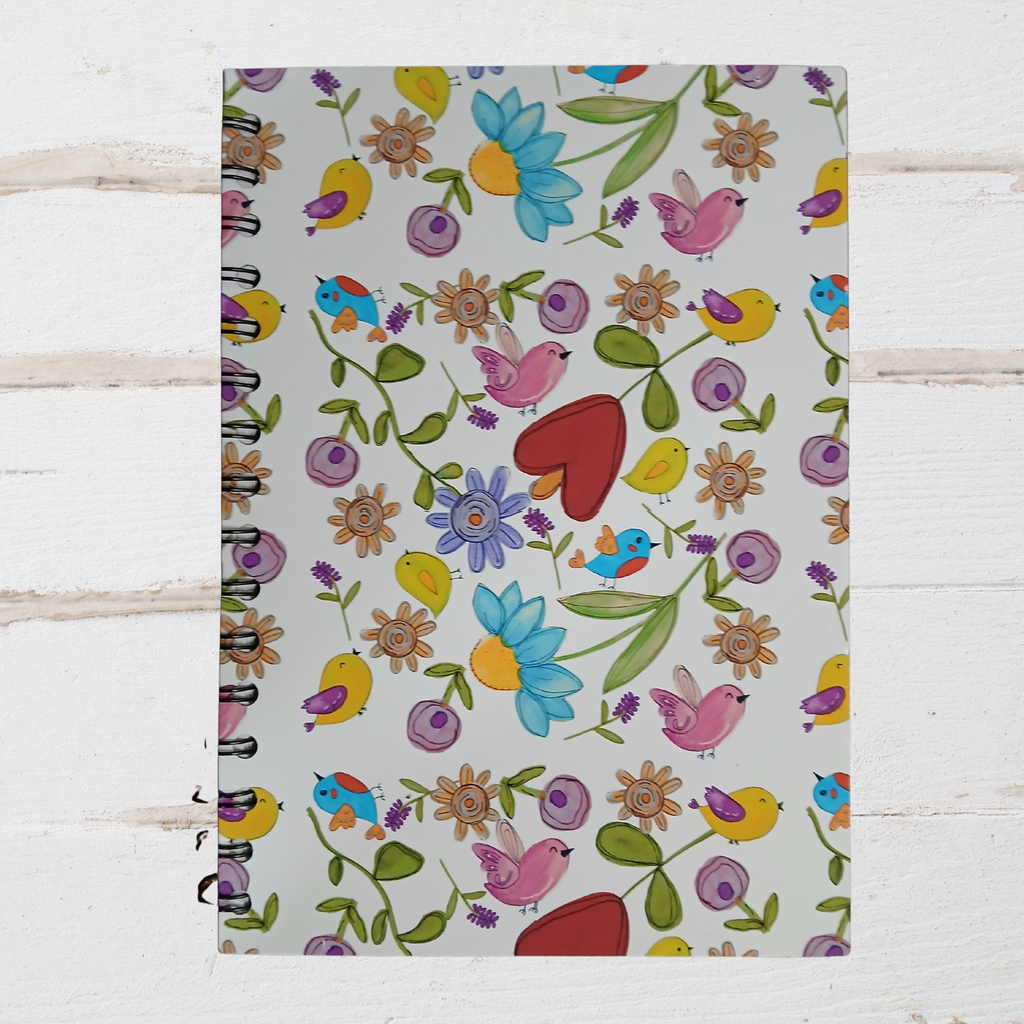 Notebook with colorful floral and bird pattern on a white wooden surface