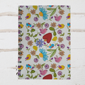 Notebook with colorful floral and bird pattern on a white wooden surface