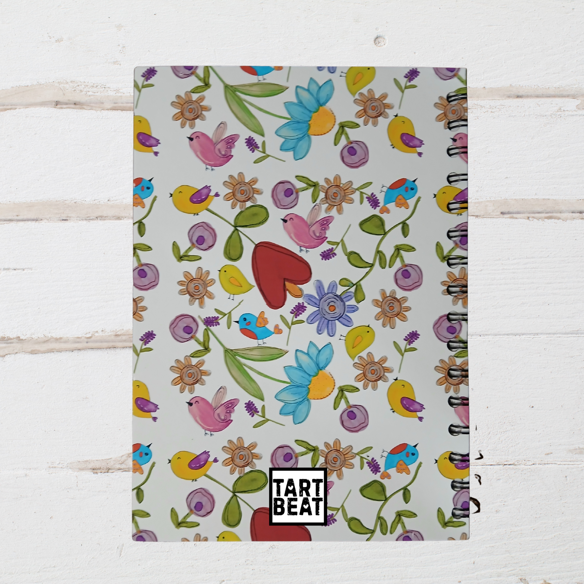 Notebook with colorful floral and bird pattern on a white wooden surface
