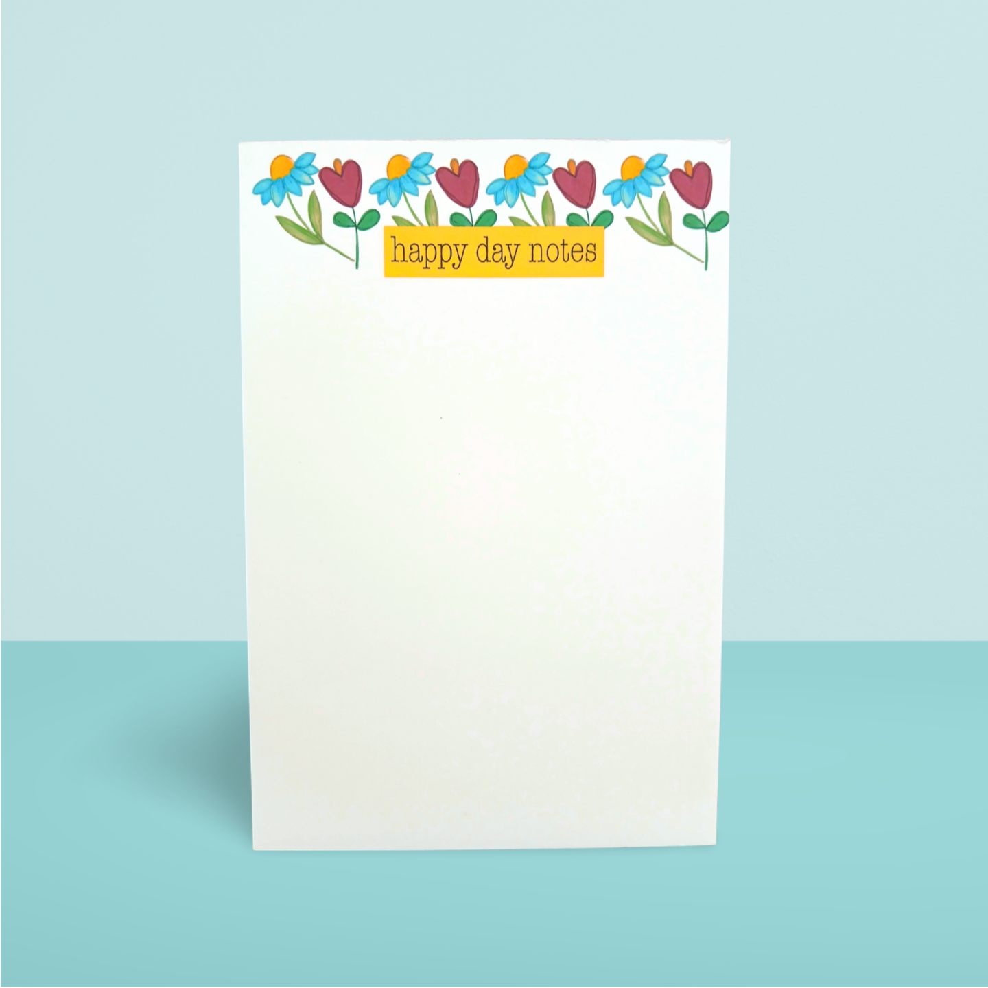 Notepad with colorful floral design and 'happy day notes' text on a light blue background
