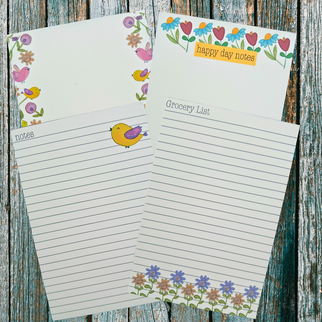 Four floral and bird decorated notepads on a wooden background