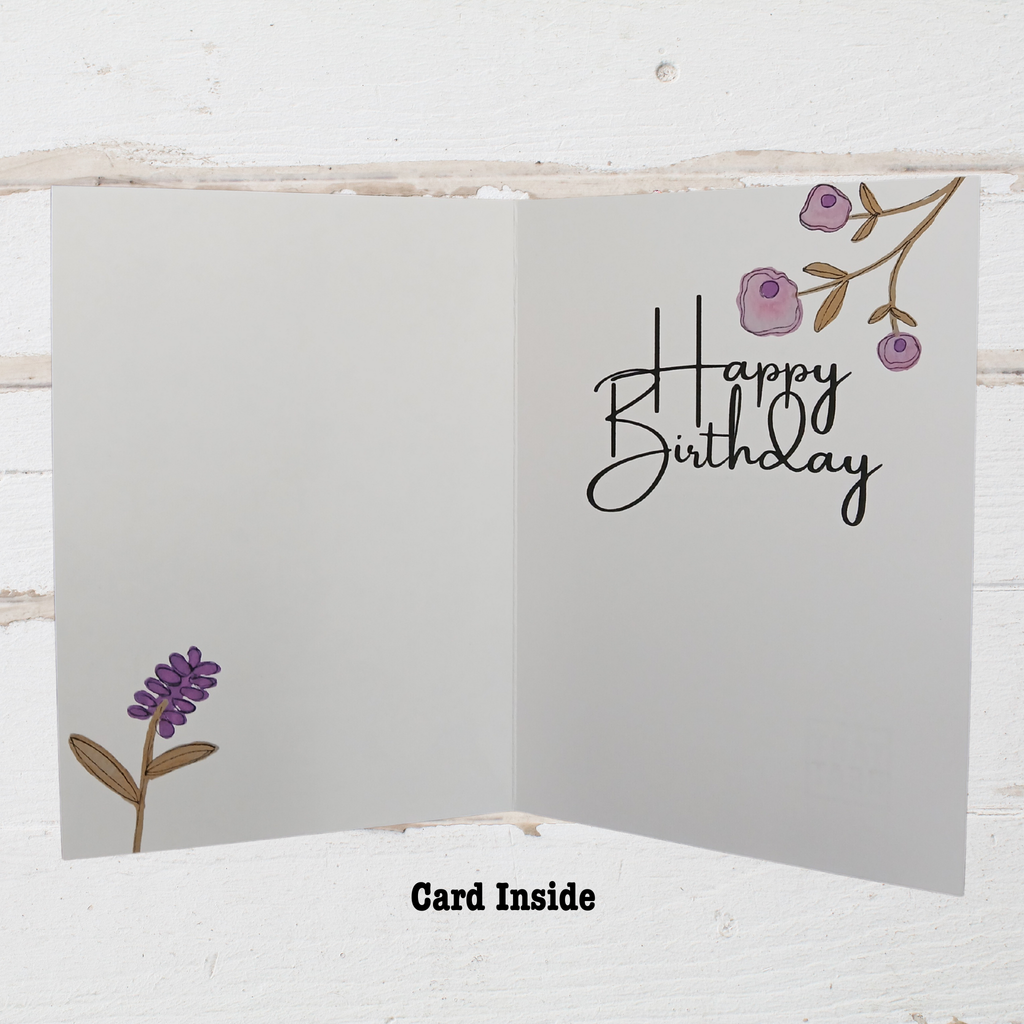 Open birthday card with 'Happy Birthday' text and floral designs on a white wooden background.