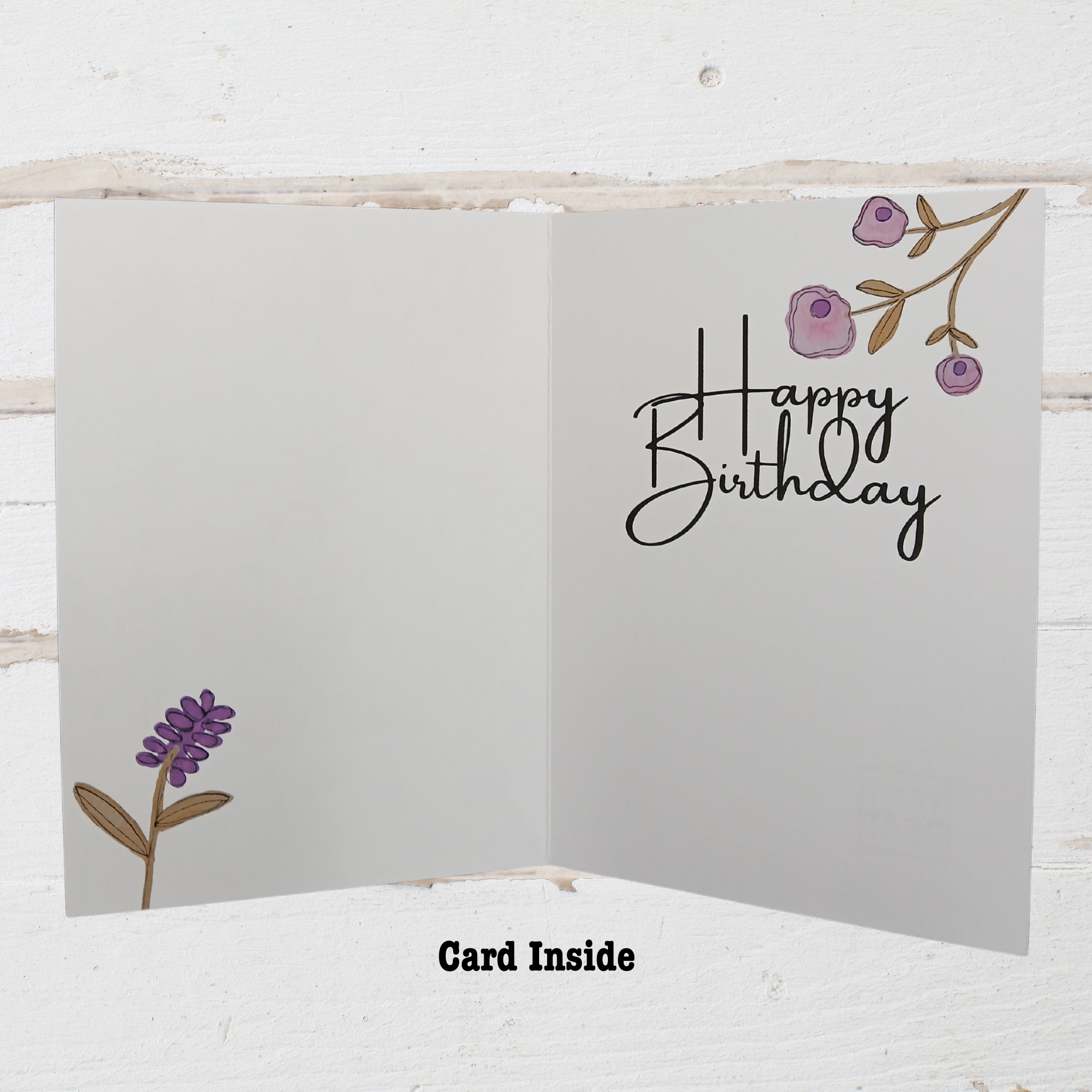 Open birthday card with 'Happy Birthday' text and floral designs on a white wooden background.