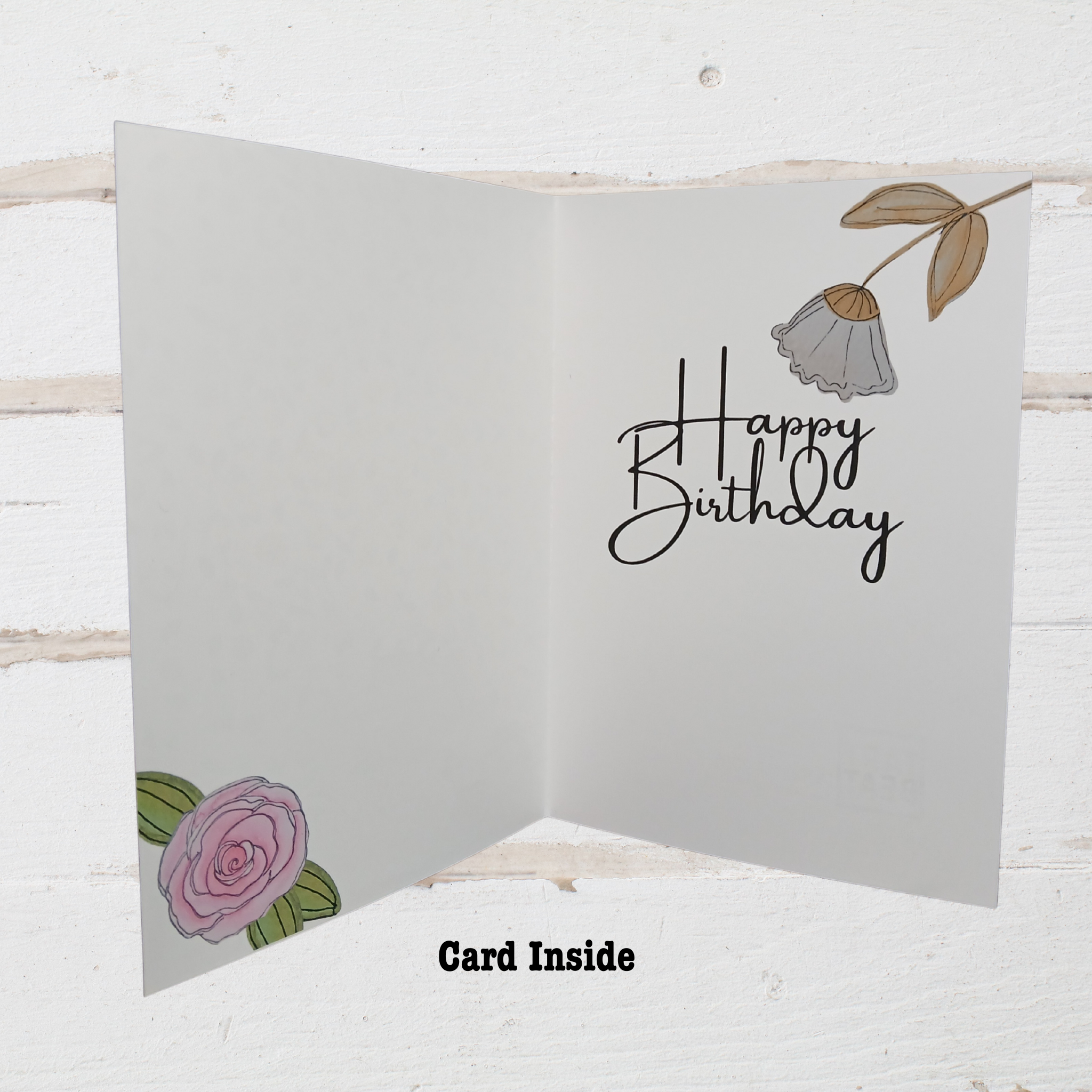 Gray birthday card with floral designs and 'Happy Birthday' text on a white wooden background
