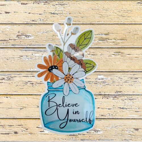 Decorative sticker with flowers and 'Believe in Yourself' text on a wooden background