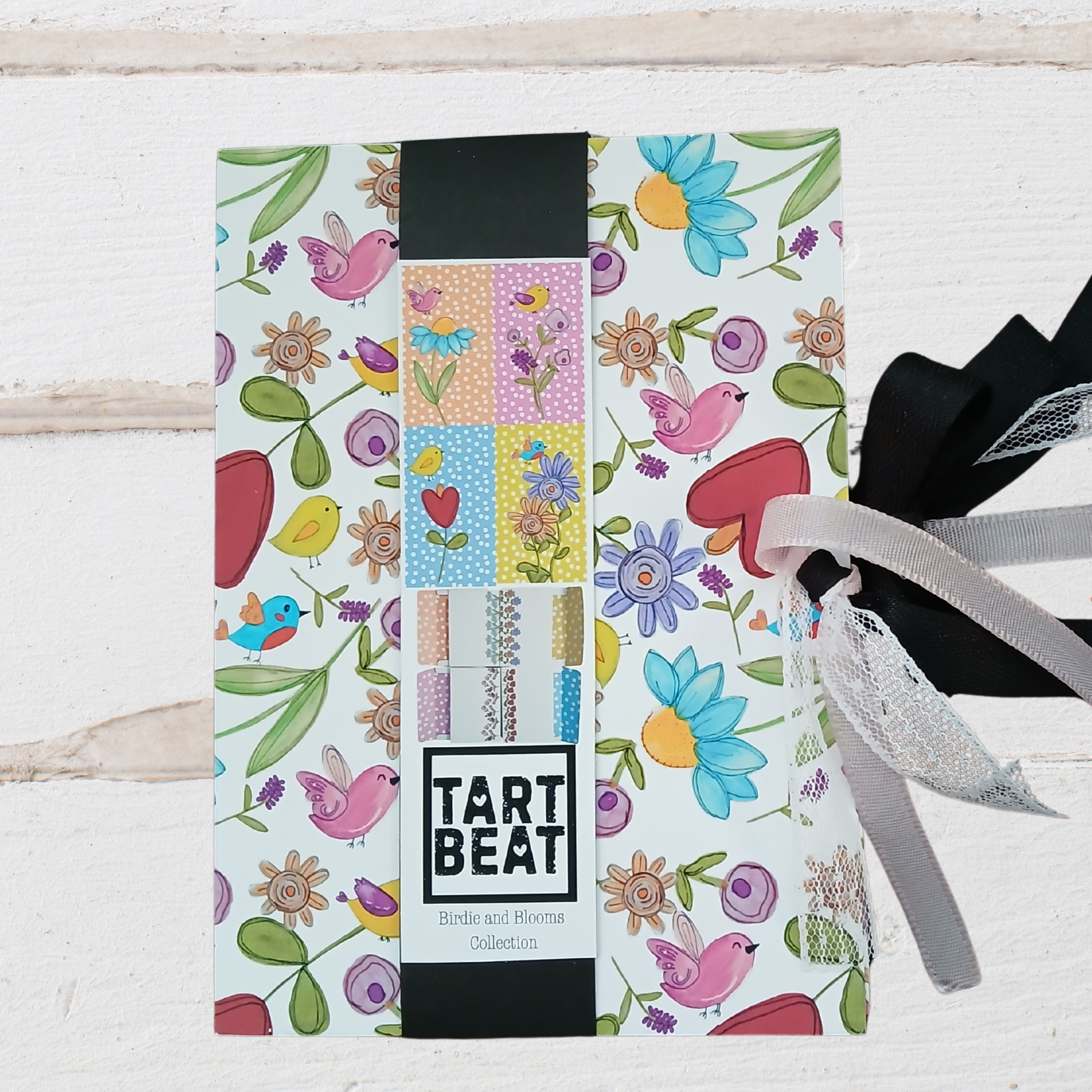 Packaging of Tart Beat stationery items with floral and bird designs on a light wooden background.