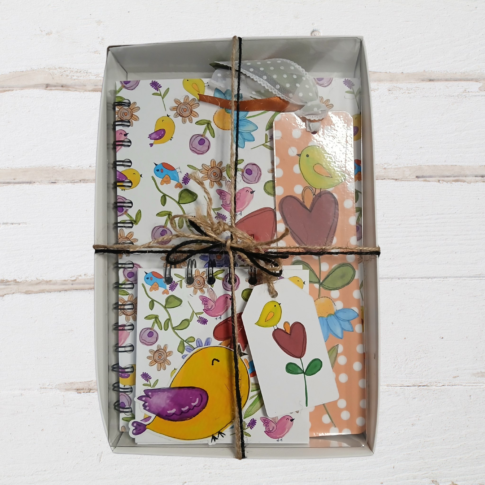 Set of stationery items including a notebook, cards, and a tag with floral and bird designs, tied together.