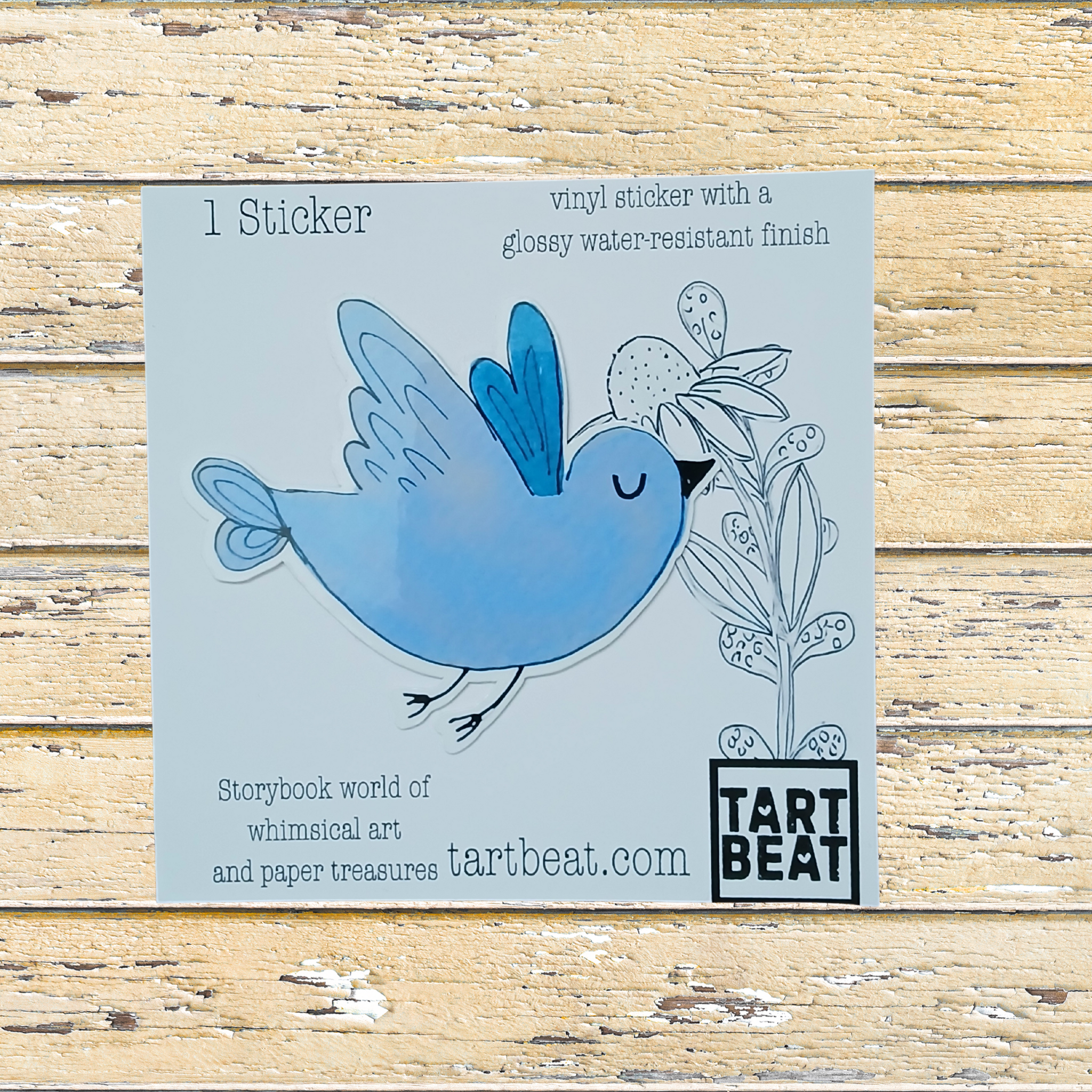 Blue bird sticker on a cardboard backing with 'Tart Beat' branding, on a wooden surface.