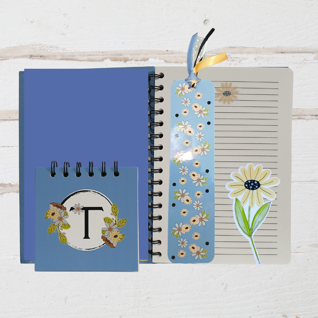 Blue notebook with floral design, bookmark, and sticker on a wooden surface