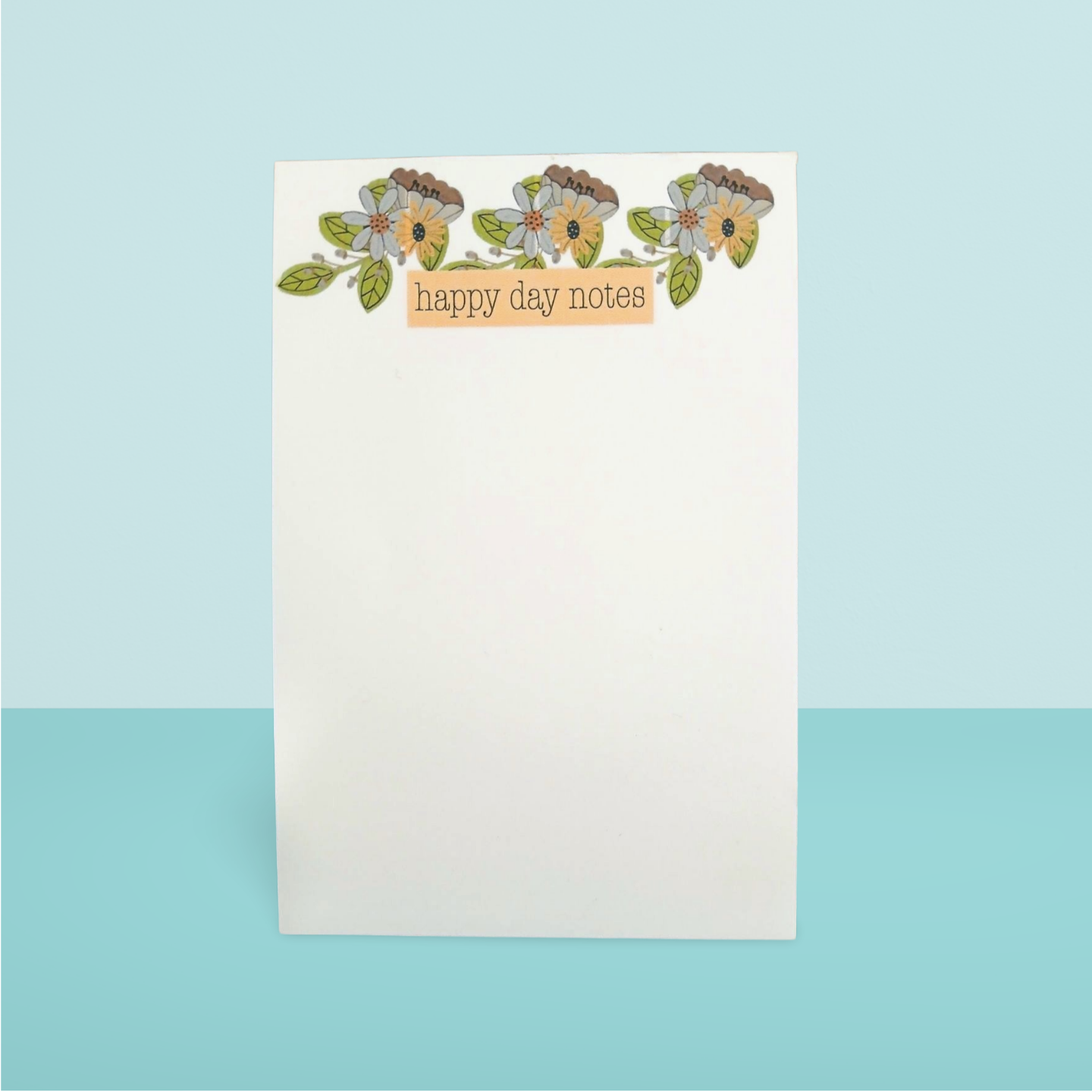 Notepad with floral design and 'happy day notes' text on a light blue background