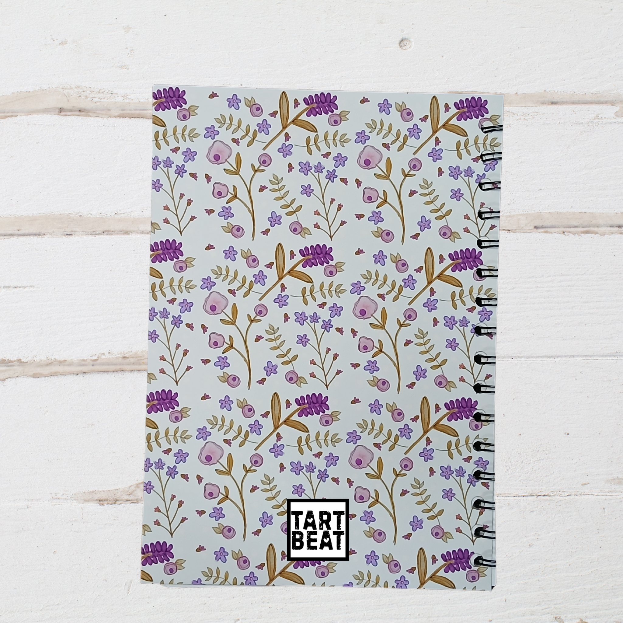 Notebook with floral pattern and 'Tart Beat' branding on a light wooden surface