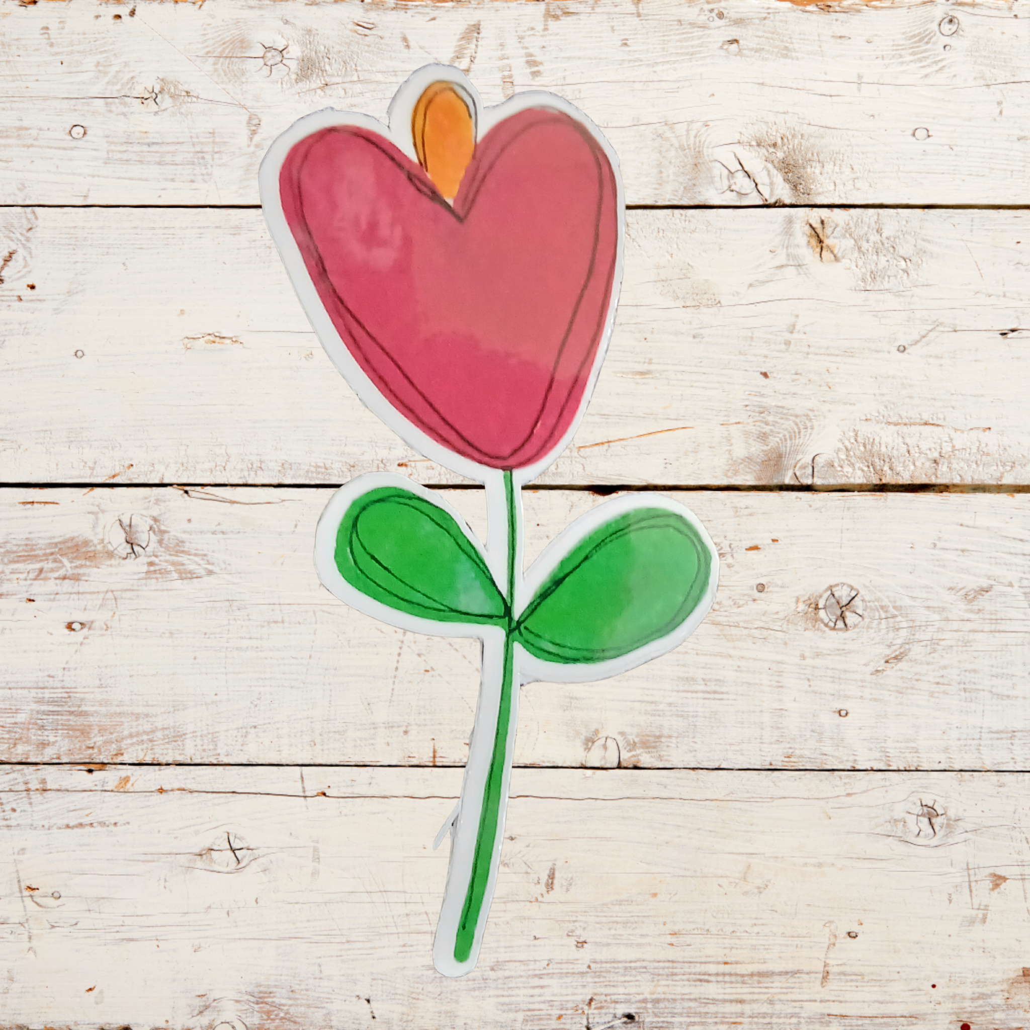 Heart-shaped flower with green stem and leaves on a wooden surface