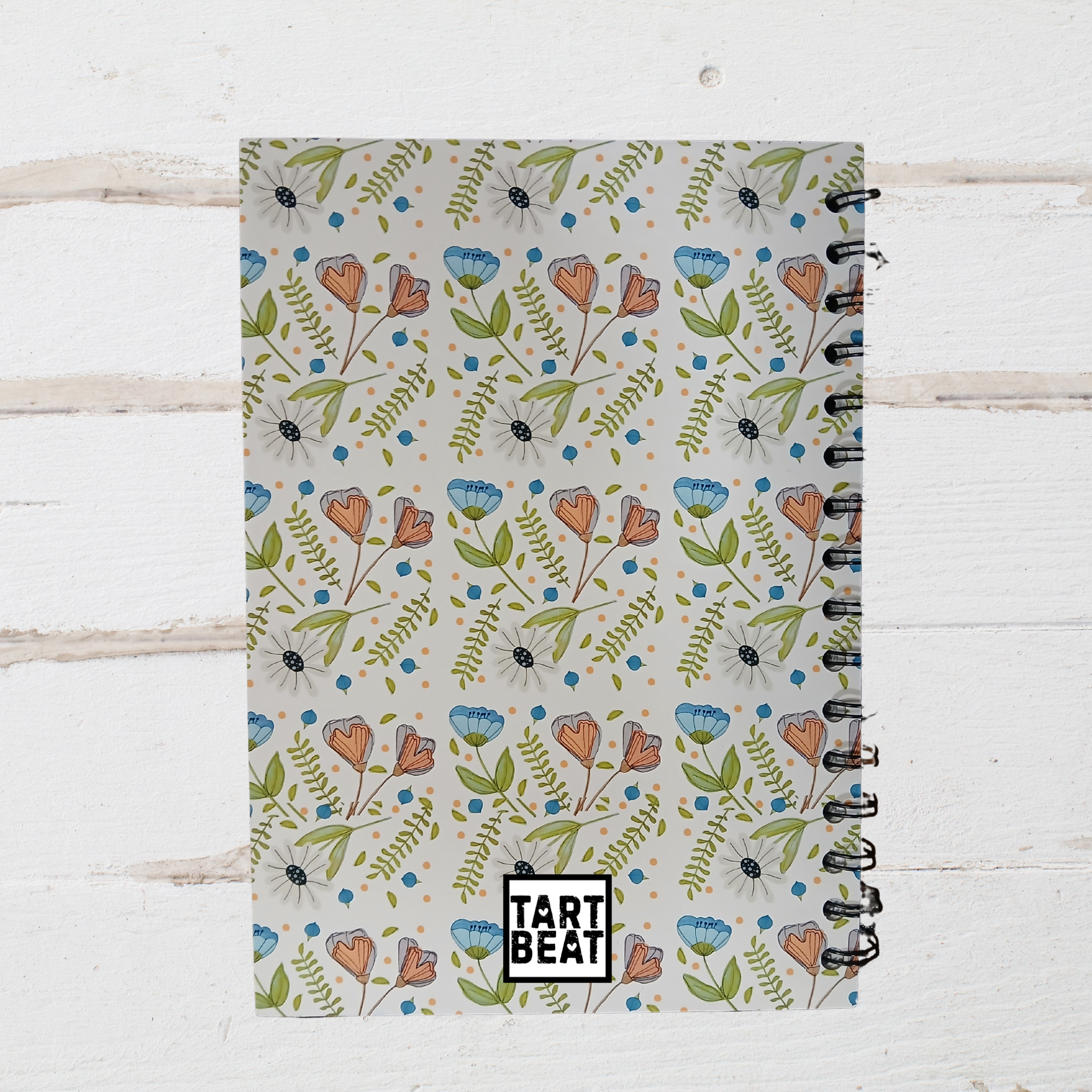 Notebook with floral pattern and 'Tart Beat' branding on a wooden surface