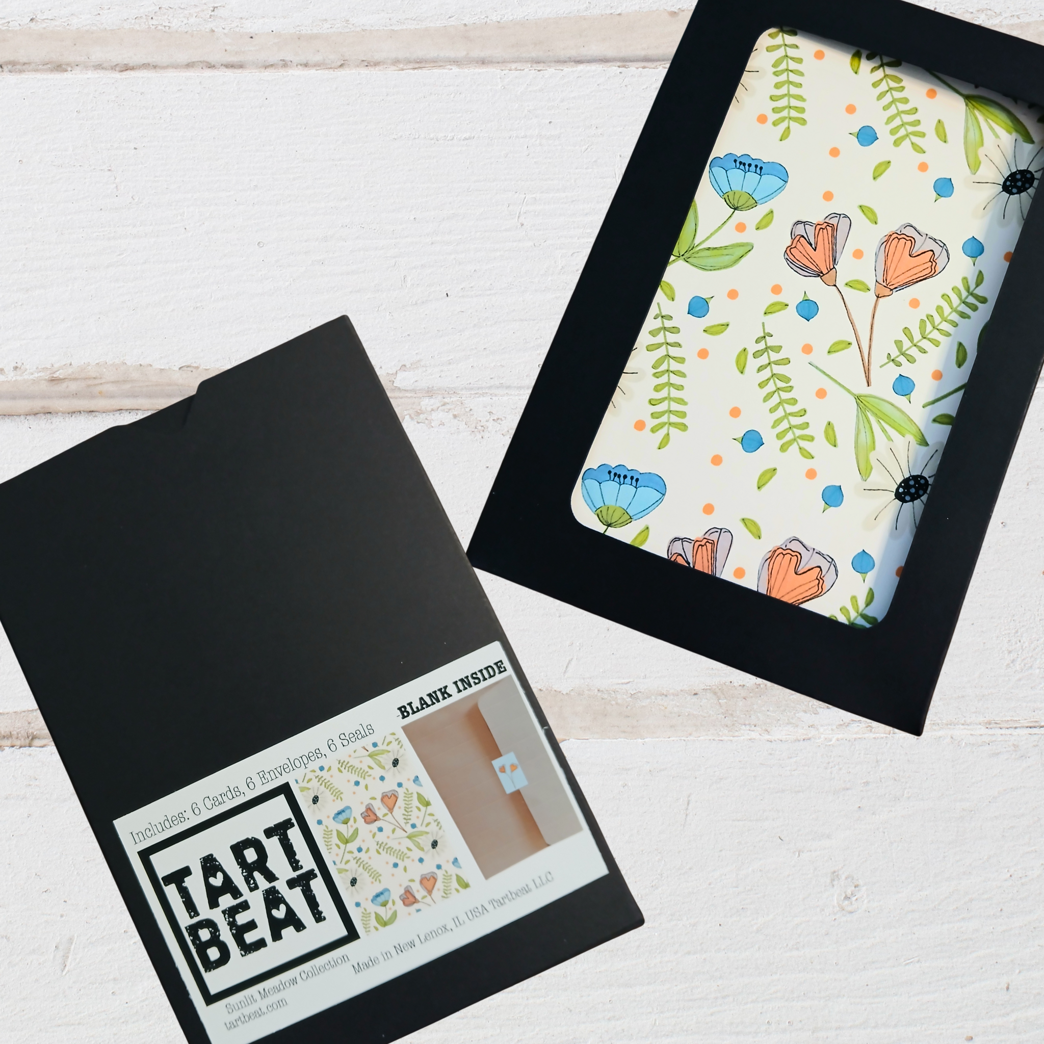 Floral-patterned card in a black frame with 'Tart Beat' packaging on a light wooden surface.