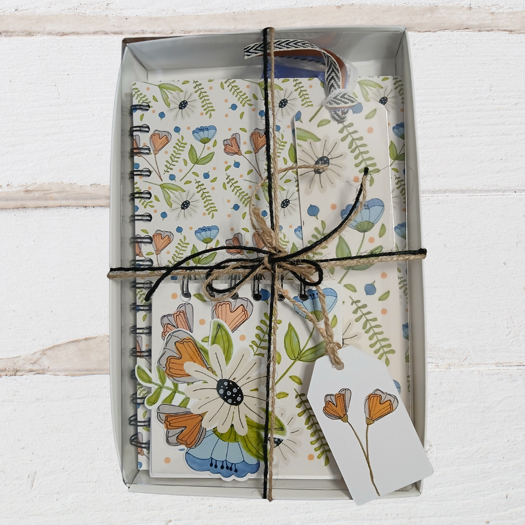 Floral notebook and card set tied with string in a box on a white wooden surface
