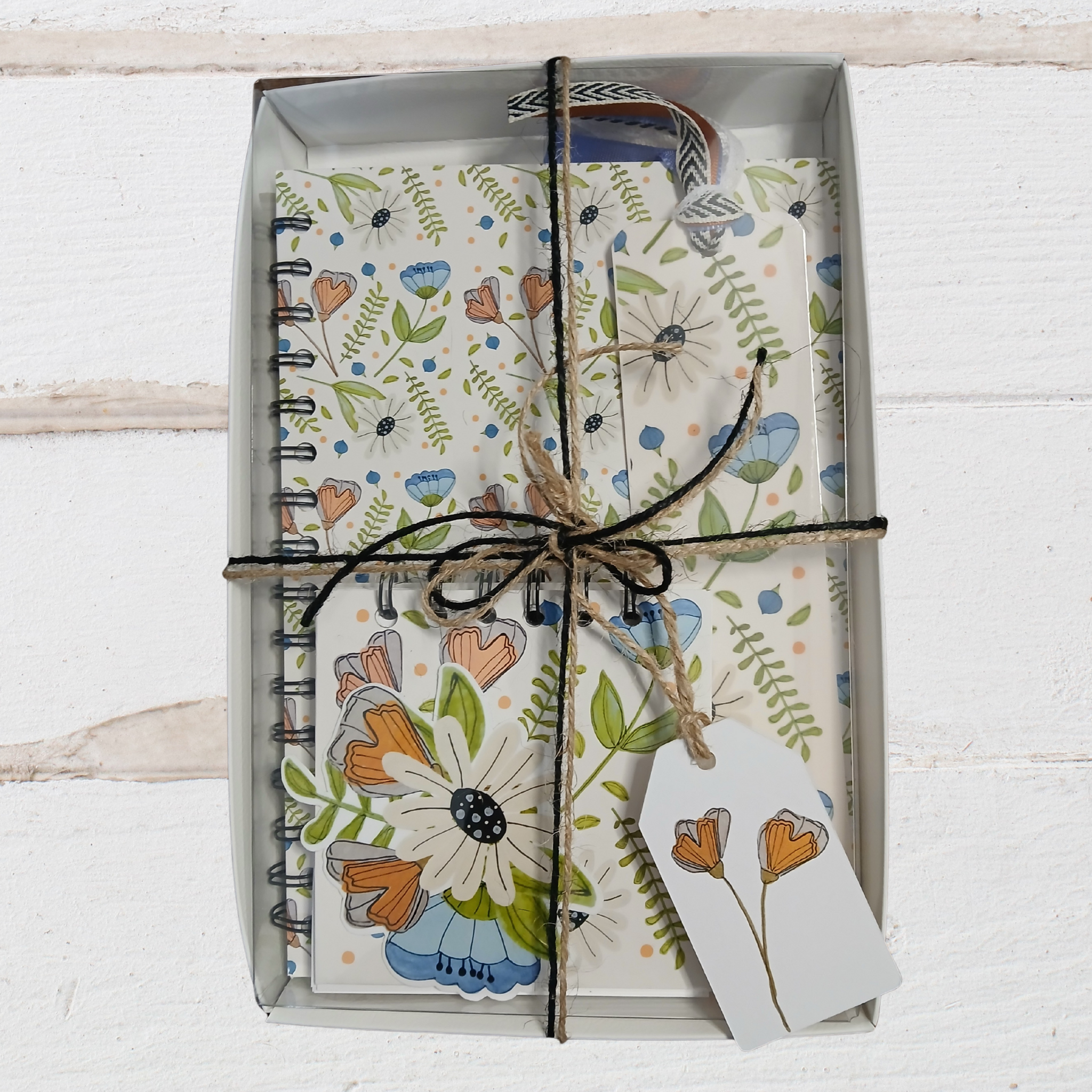 Floral notebook and card set tied with string in a box on a white wooden surface